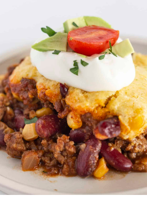 Chili cornbread casserole topped with sour cream, avocado, and tomato, a flavorful comfort casseroles dish perfect for easy comfort food and recipes for busy nights.