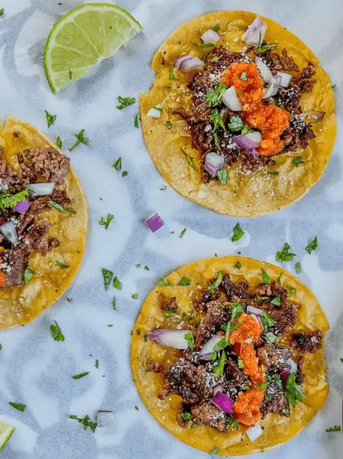 Crispy beef smash tacos on yellow corn tortillas topped with charred ground chuck, homemade hot sauce, red onion, cotija cheese, and fresh cilantro — an easy Cinco de Mayo party food recipe for a crowd that makes 10 tacos in under 30 minutes of active cooking time.