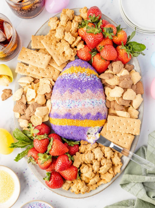 Easter dessert charcuterie board with a colorful egg-shaped cheese ball surrounded by strawberries, crackers, cookies, and snacks, a festive no-bake Easter-themed dessert for a bake sale.