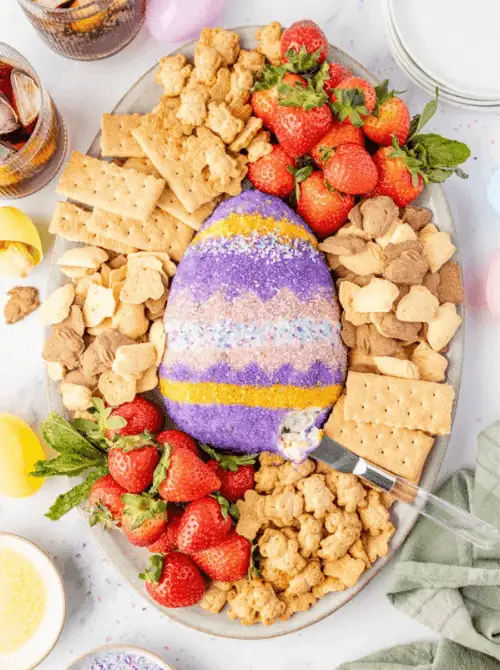 Easter dessert charcuterie board with a colorful egg-shaped cheese ball surrounded by strawberries, crackers, cookies, and snacks, a festive no-bake Easter-themed dessert for a bake sale.