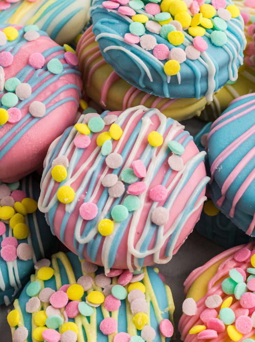 Pastel chocolate-covered no-bake Easter-themed desserts for a bake sale, featuring colorful dipped treats drizzled with pink and white icing and topped with festive Easter sprinkles.