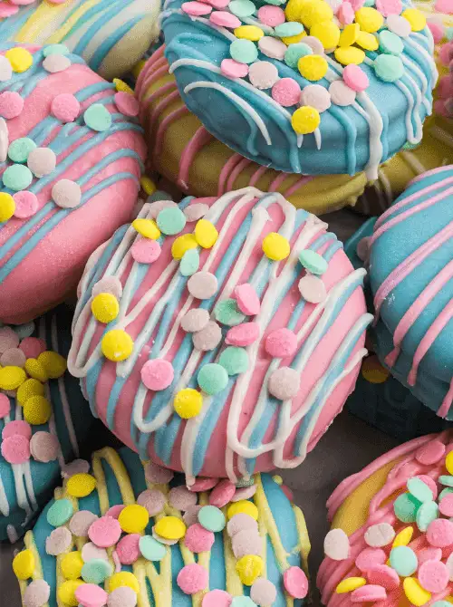 Pastel chocolate-covered no-bake Easter-themed desserts for a bake sale, featuring colorful dipped treats drizzled with pink and white icing and topped with festive Easter sprinkles.