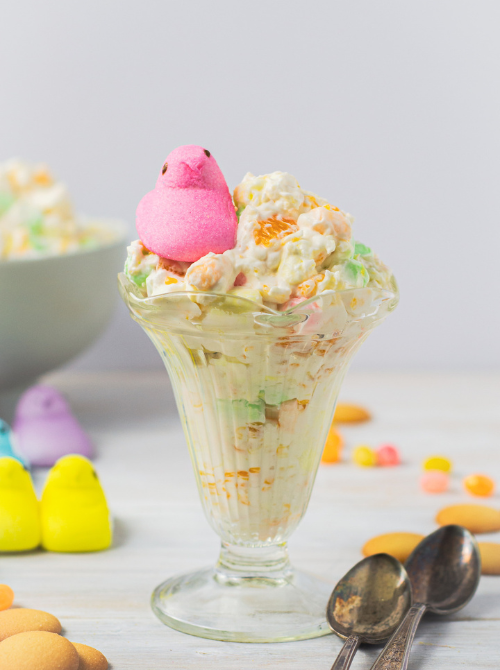 Glass dish of creamy no-bake Easter-themed dessert for a bake sale, topped with popcorn, pastel candy pieces, and a pink marshmallow chick for a festive spring treat.