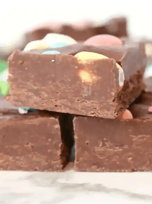 Stack of rich chocolate no-bake Easter-themed dessert fudge squares for a bake sale, topped with pastel candy eggs and cut into thick, festive dessert bars.