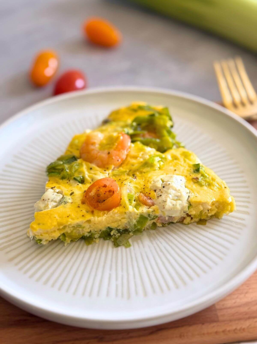 Slice of shrimp and leek frittata with cherry tomatoes served on a plate, a light seafood option that works well in make-ahead Easter brunch casseroles.