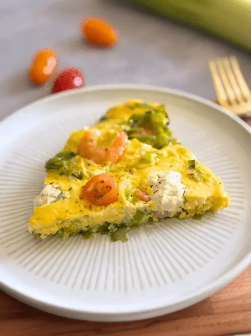 Slice of shrimp and leek frittata with cherry tomatoes served on a plate, a light seafood option that works well in make-ahead Easter brunch casseroles.