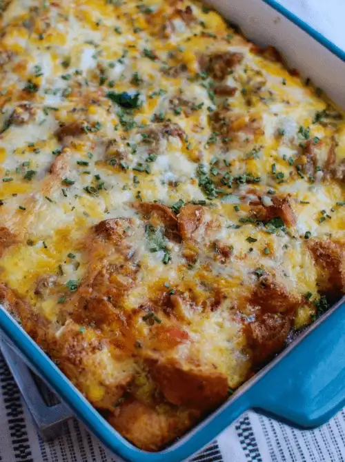 Cheesy sausage and egg breakfast casserole baked in a blue dish with herbs sprinkled on top, a hearty option for make-ahead Easter brunch casseroles perfect for feeding a crowd.