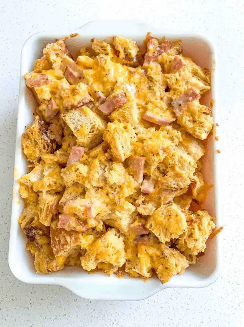 Ham and cheese breakfast casserole with toasted bread cubes baked in a white dish, a hearty comfort food option for make-ahead Easter brunch casseroles.