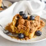 Make-ahead Easter brunch casserole slice served on a white plate, topped with fresh blueberries and crumb topping, perfect for a sweet holiday breakfast.