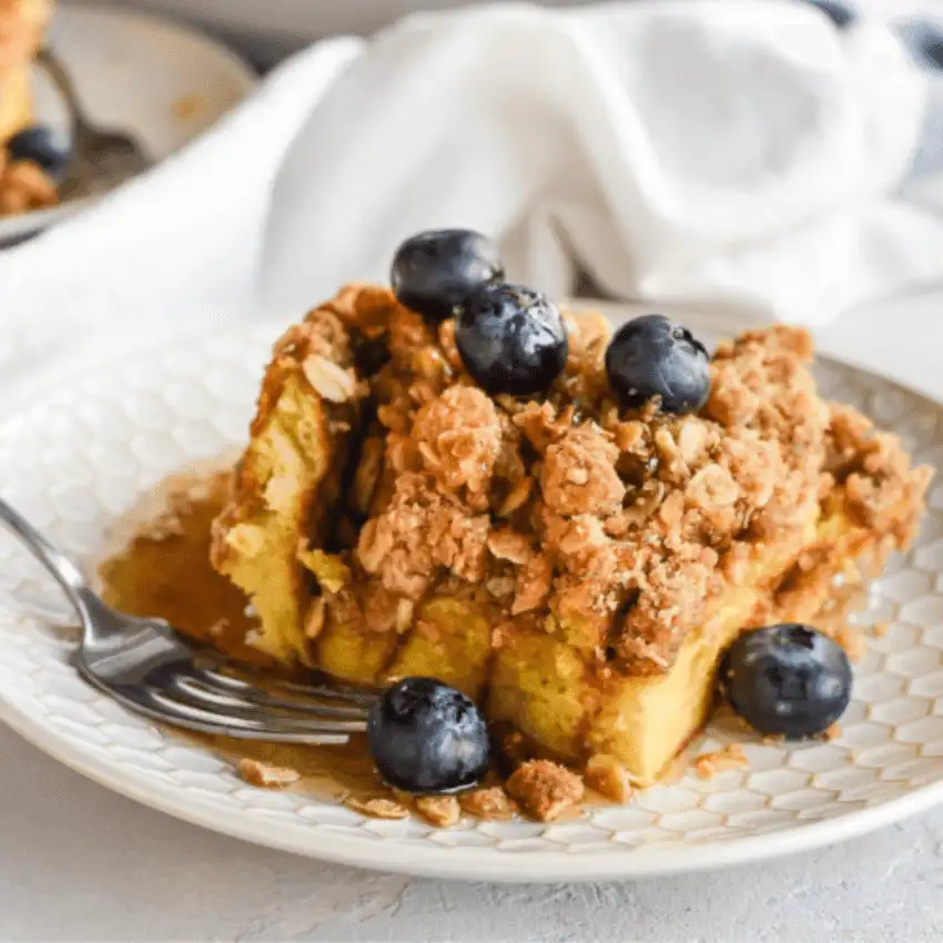Make-ahead Easter brunch casserole slice served on a white plate, topped with fresh blueberries and crumb topping, perfect for a sweet holiday breakfast.