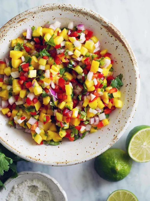 Easy Cinco de Mayo party food recipes for a crowd featuring a vibrant bowl of fresh mango salsa with diced mango, red onion, jalapeño, cilantro, and lime on a light marble surface.