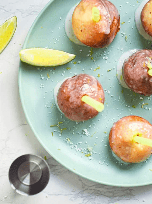 Bite-sized margarita cake pops with tequila glaze, coarse sea salt, and lime zest on a mint green plate — an easy Cinco de Mayo party food recipe for a crowd that makes 48 boozy dessert bites for under $0.35 each.