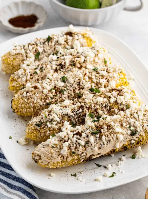 Grilled Mexican street corn on the cob topped with cotija cheese, chili powder, and cilantro on a white serving platter — one of the most popular easy Cinco de Mayo party food recipes for a crowd.