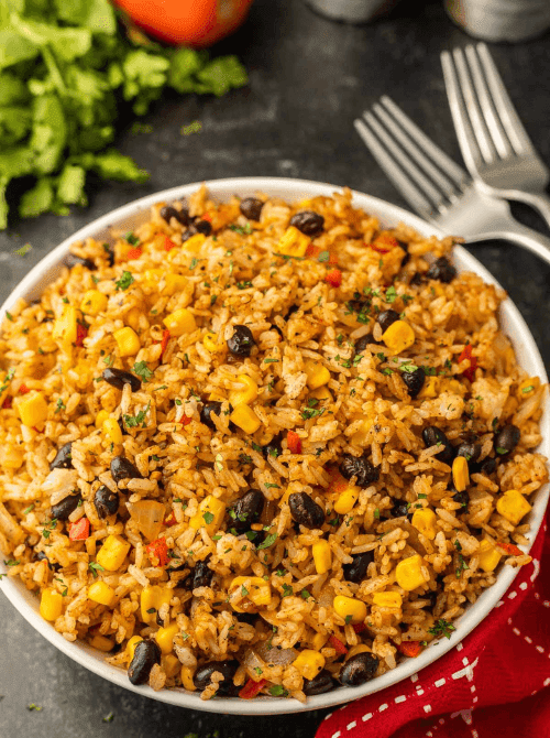 Blackstone Mexican fried rice in a large white bowl with black beans, corn, red bell pepper, and cilantro in a smoky enchilada sauce — an easy Cinco de Mayo party food recipe for a crowd that's ready in just 25 minutes and stores well for up to 5 days.