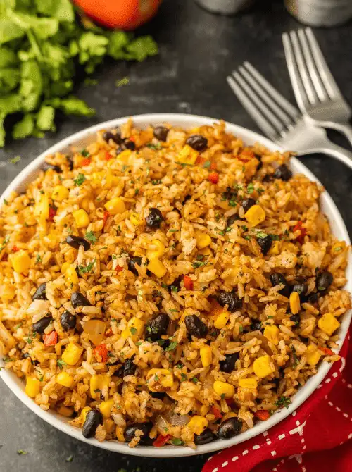 Blackstone Mexican fried rice in a large white bowl with black beans, corn, red bell pepper, and cilantro in a smoky enchilada sauce — an easy Cinco de Mayo party food recipe for a crowd that's ready in just 25 minutes and stores well for up to 5 days.