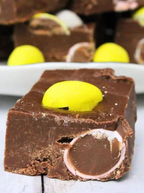 Square of rich chocolate no-bake Easter-themed dessert fudge for a bake sale, topped with a yellow candy and filled with chocolate candy pieces inside the thick fudge bar.