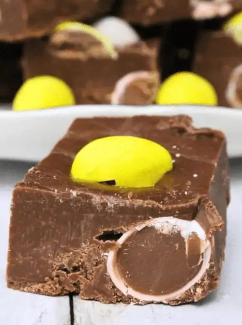 Square of rich chocolate no-bake Easter-themed dessert fudge for a bake sale, topped with a yellow candy and filled with chocolate candy pieces inside the thick fudge bar.