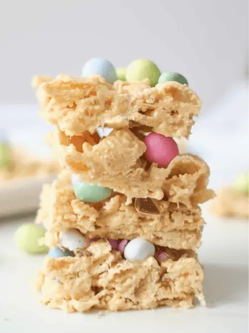 Stack of crunchy no-bake Easter-themed dessert bars for a bake sale, made with cereal treats and mixed with pastel chocolate eggs and candy pieces for a festive spring sweet.