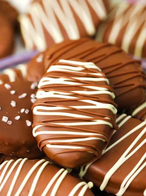 Chocolate-covered no-bake Easter-themed desserts for a bake sale, featuring oval-shaped Easter egg treats coated in chocolate and drizzled with white chocolate for a festive spring dessert.