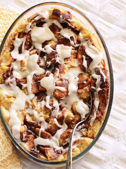 Cinnamon roll bread pudding casserole with creamy icing drizzle baked in a glass dish, a sweet and cozy option for make-ahead Easter brunch casseroles.