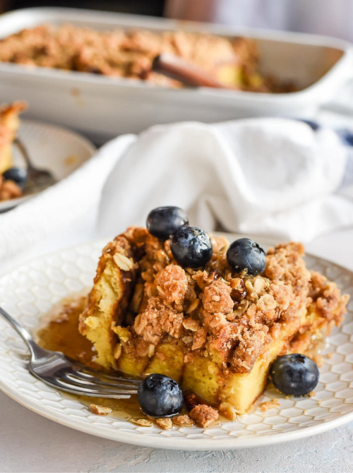 Slice of baked French toast casserole topped with crunchy streusel and fresh blueberries on a plate, a sweet option for make-ahead Easter brunch casseroles served with maple syrup.