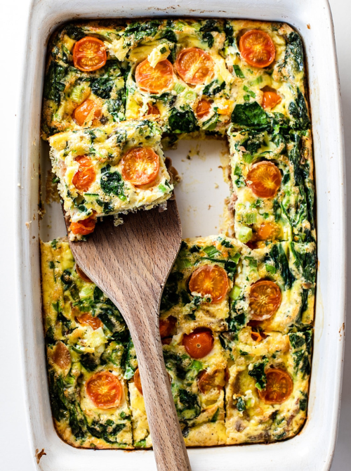 Spinach, tomato, and egg breakfast casserole baked in a white dish with a slice being served, a fresh veggie-packed option for make-ahead Easter brunch casseroles.