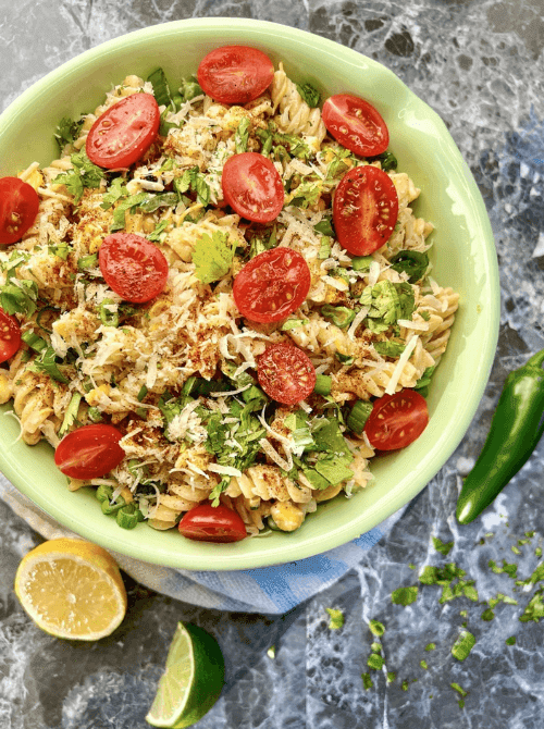 Street corn pasta salad in a green bowl with rotini, cherry tomatoes, roasted corn, cilantro, and parmesan — a make-ahead easy Cinco de Mayo party food recipe for a crowd that serves 8 and gets better as it chills.
