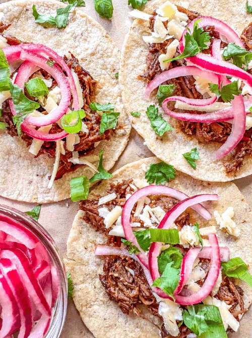 Tacos de barbacoa on corn tortillas topped with slow-cooked shredded beef, pickled red onions, white cheddar, and fresh cilantro — an easy Cinco de Mayo party food recipe for a crowd that feeds 8 with just 10 minutes of prep.