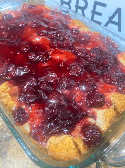 A glass baking dish of cherry cheesecake monkey bread casserole topped with glossy cherry pie filling over golden baked biscuit pieces — a show-stopping make-ahead Mother's Day brunch idea made with canned biscuits that assembles in 15 minutes and costs about six dollars to make.