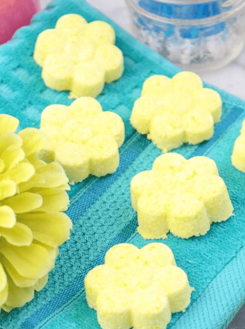 4:34 AMYellow flower-shaped DIY shower steamers arranged on a teal towel with a yellow paper flower — a handmade aromatherapy spa gift idea for DIY Mother's Day gift baskets.