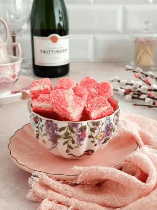 Pink and white no-bake coconut ice squares served in a floral teacup on a pink saucer — a pretty homemade sweet treat idea for DIY Mother's Day gift baskets.