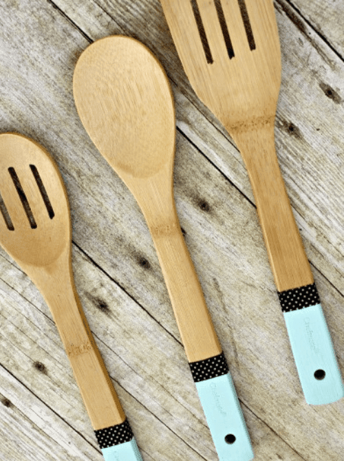 Three wooden kitchen utensils with mint green color-dipped handles and polka dot washi tape accents on a rustic wood surface — a practical and pretty handmade kitchen gift for DIY Mother's Day gift baskets.