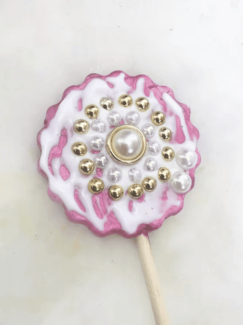 A handmade air dry clay flower plant poke in pink and white with pearl and gold rhinestone embellishments on a wooden dowel — a decorative homemade garden gift for DIY Mother's Day gift baskets.