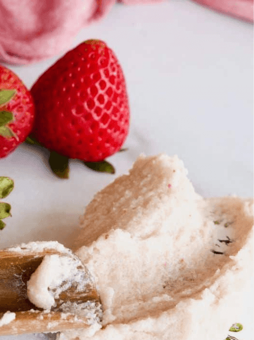 Strawberry DIY sugar scrub on a wooden spoon with fresh strawberries in the background — a handmade bath and beauty idea for DIY Mother's Day gift baskets.