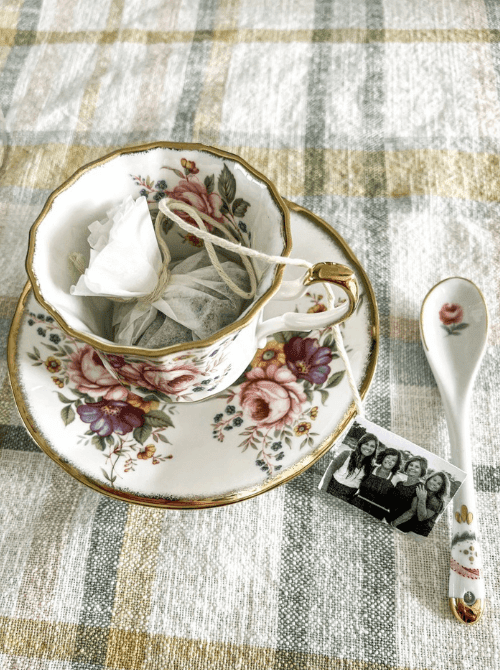 Homemade DIY tea bags with a personal photo tag resting in a vintage floral teacup and saucer — a sentimental and budget-friendly handmade gift idea for DIY Mother's Day gift baskets.
