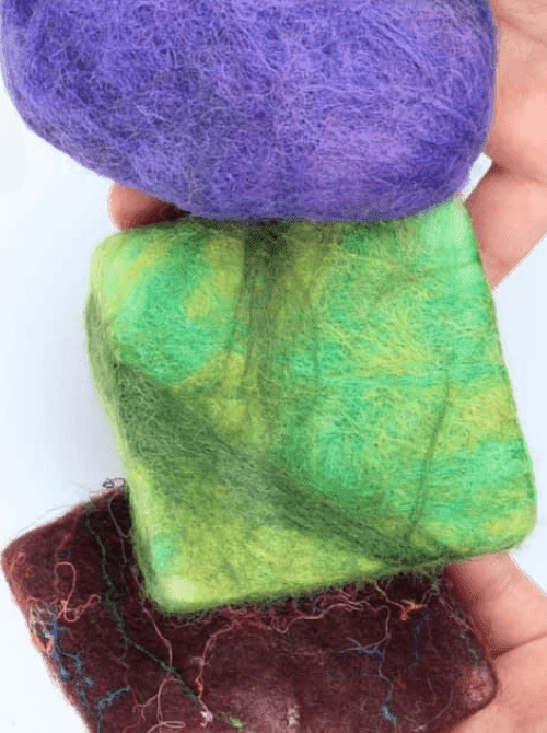 Three handmade felted soap bars in purple, green, and burgundy wool held in a hand — a unique and long-lasting handmade bath gift idea for DIY Mother's Day gift baskets.
