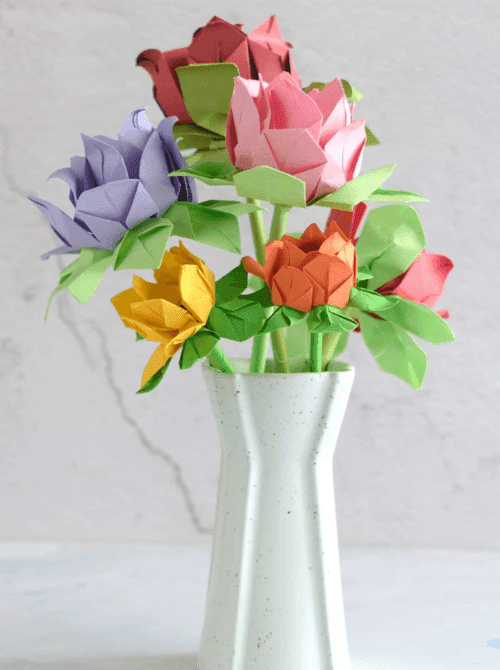 A bouquet of colorful handmade paper roses in purple, pink, red, orange, and yellow displayed in a white ceramic vase — a no-wilt handmade keepsake for DIY Mother's Day gift baskets.