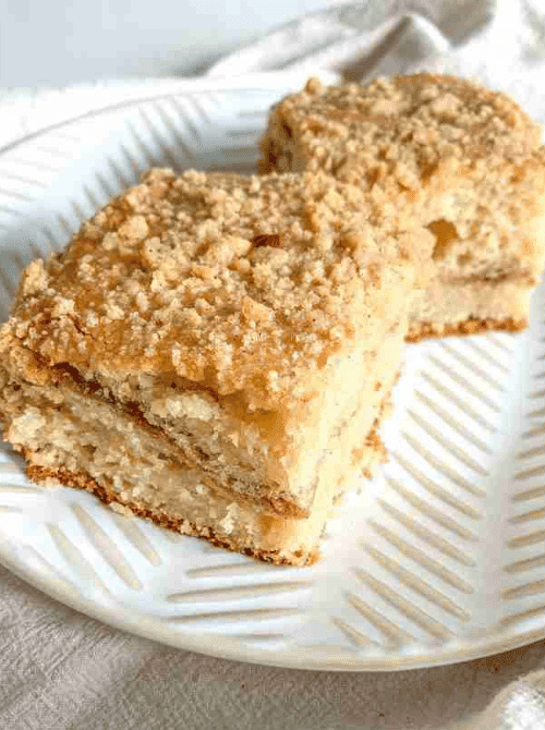 Two squares of sourdough coffee cake with a visible cinnamon swirl layer and golden buttery streusel topping stacked on a white textured plate — a wholesome make-ahead Mother's Day brunch idea sweetened with maple syrup instead of refined sugar that can be mixed the night before and baked fresh in the morning.