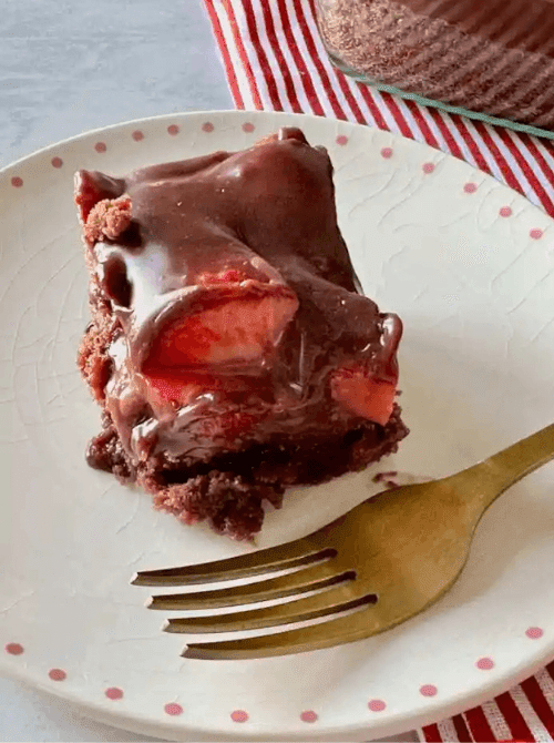 A single slice of chocolate covered strawberry brownie on a white polka dot plate with a gold fork, showing fresh strawberries under a drizzle of chocolate ganache — an easy strawberry dessert recipe that works for weeknights and company alike.