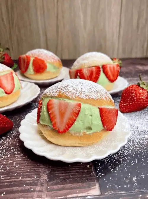 Soft cream buns filled with matcha cream and fresh strawberry slices, dusted with powdered sugar on white plates — an impressive fresh strawberry brunch recipe for a special occasion.
