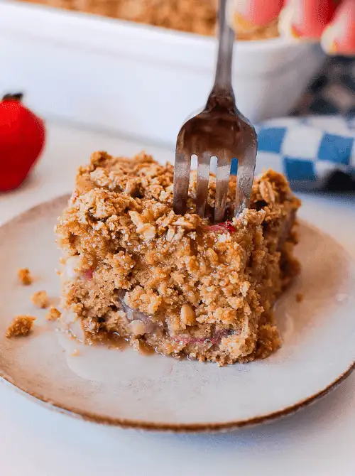 Fork pressing into a square slice of gluten-free strawberry coffee cake with thick oat crumble topping and visible strawberry filling on a ceramic plate — a from-scratch strawberry cake recipe that works as breakfast or dessert
