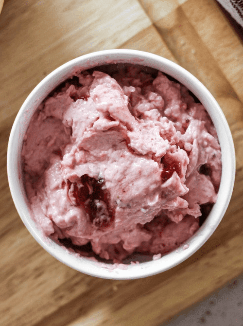 Overhead view of homemade strawberry cream cheese spread in a white bowl on a wooden cutting board — a 5-minute make-ahead fresh strawberry brunch recipe for bagels and scones.