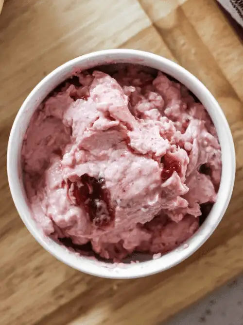 Overhead view of homemade strawberry cream cheese spread in a white bowl on a wooden cutting board — a 5-minute make-ahead fresh strawberry brunch recipe for bagels and scones.