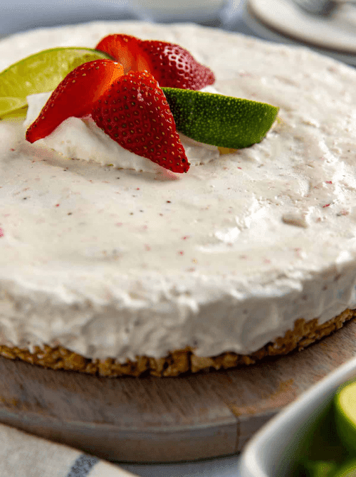 A whole frozen strawberry margarita pie on a wooden board with a pretzel crust and creamy speckled filling, topped with fresh strawberry slices and lime wedges — the most refreshing summer strawberry dessert on this list and the one to reach for on the hottest days.