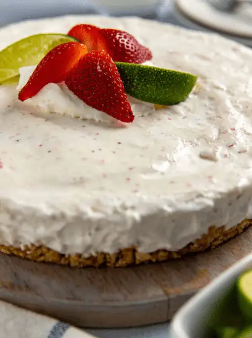 A whole frozen strawberry margarita pie on a wooden board with a pretzel crust and creamy speckled filling, topped with fresh strawberry slices and lime wedges — the most refreshing summer strawberry dessert on this list and the one to reach for on the hottest days.