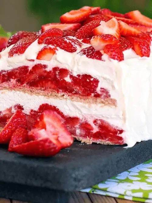 Sliced strawberry icebox cake on a slate board showing thick layers of fresh strawberries and whipped cream between graham crackers — one of the easiest no-bake strawberry cake recipes for a crowd
