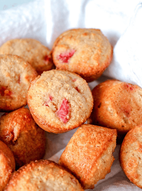 Golden baked strawberry mini muffins with visible strawberry pieces piled in a linen-lined basket — a bite-sized fresh strawberry brunch recipe for a crowd.