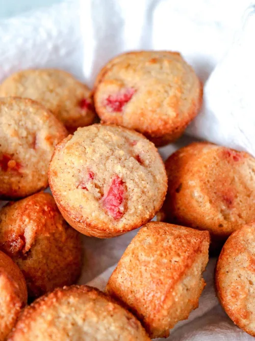 Golden baked strawberry mini muffins with visible strawberry pieces piled in a linen-lined basket — a bite-sized fresh strawberry brunch recipe for a crowd.