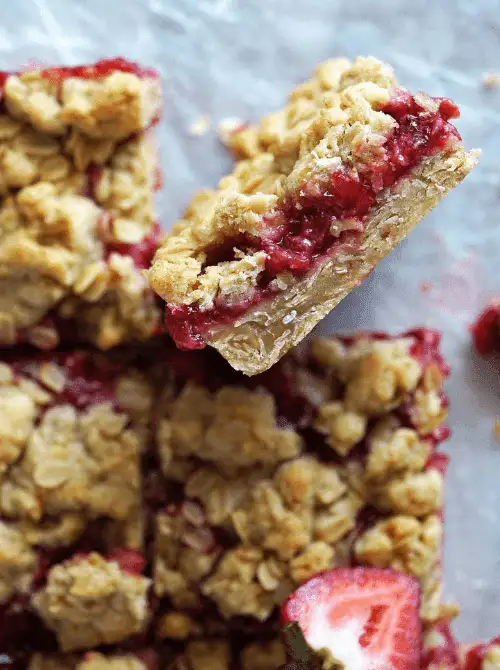 Overhead view of sliced strawberry oatmeal bars with jammy strawberry filling and buttery oat crumble topping on parchment paper — a make-ahead fresh strawberry brunch recipe that serves 16.