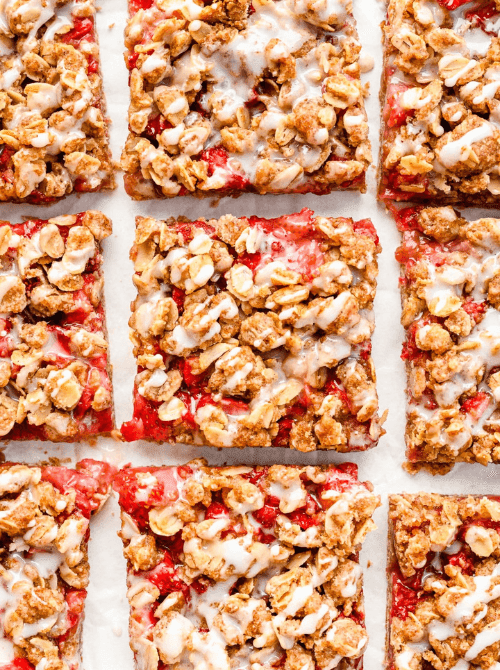 Overhead view of sliced strawberry oatmeal bars with fresh strawberry filling, oat crumble topping, and vanilla glaze arranged on parchment paper — an easy grab-and-go fresh strawberry brunch recipe.
